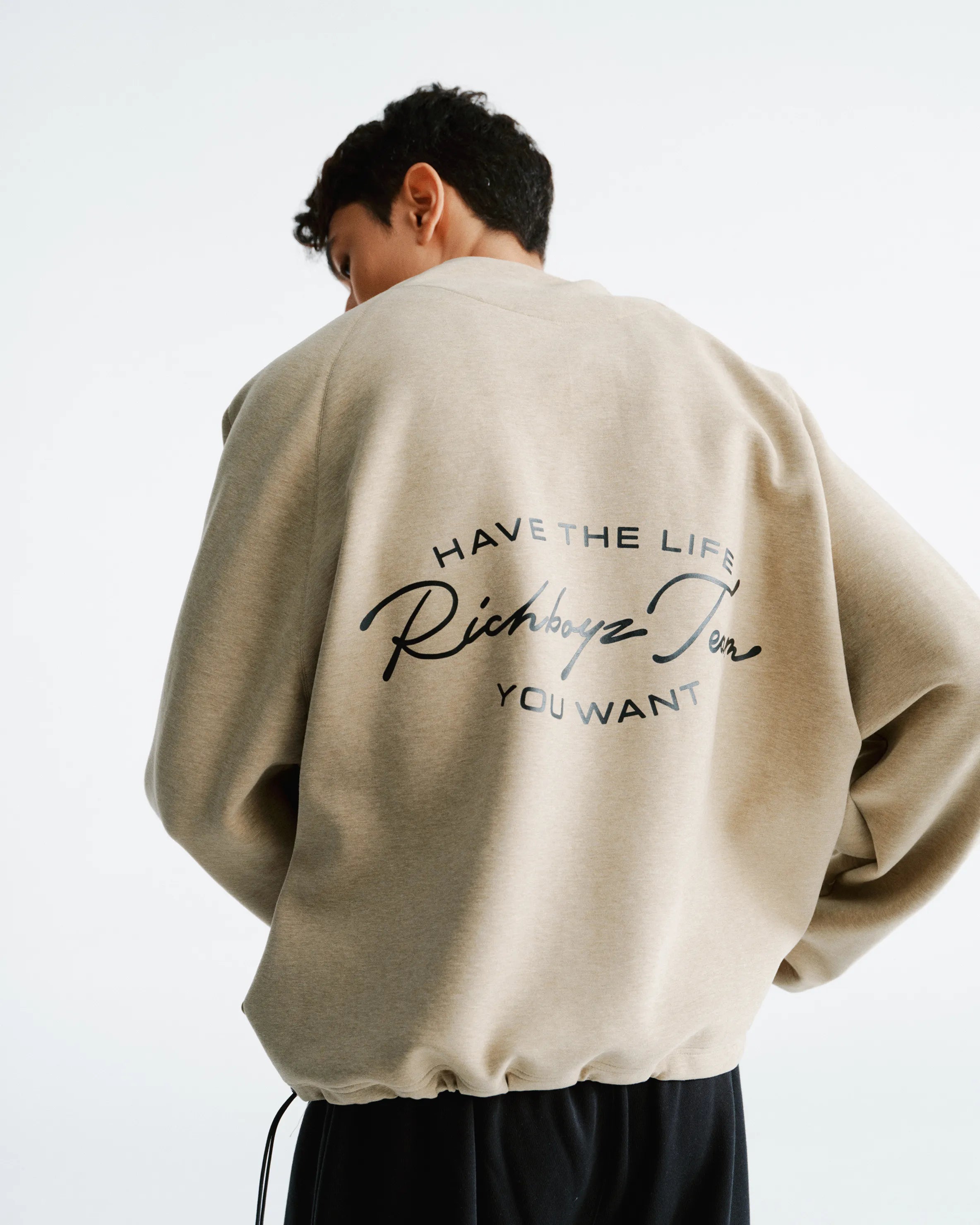 Person wearing a beige sweatshirt with text on the back against a white background