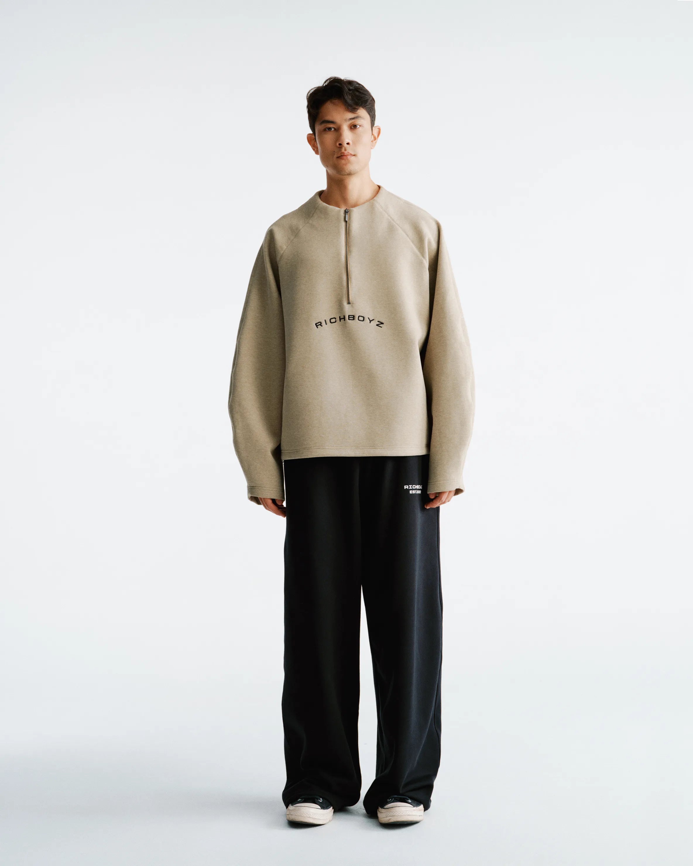 Person wearing a beige sweater and black pants on a white background
