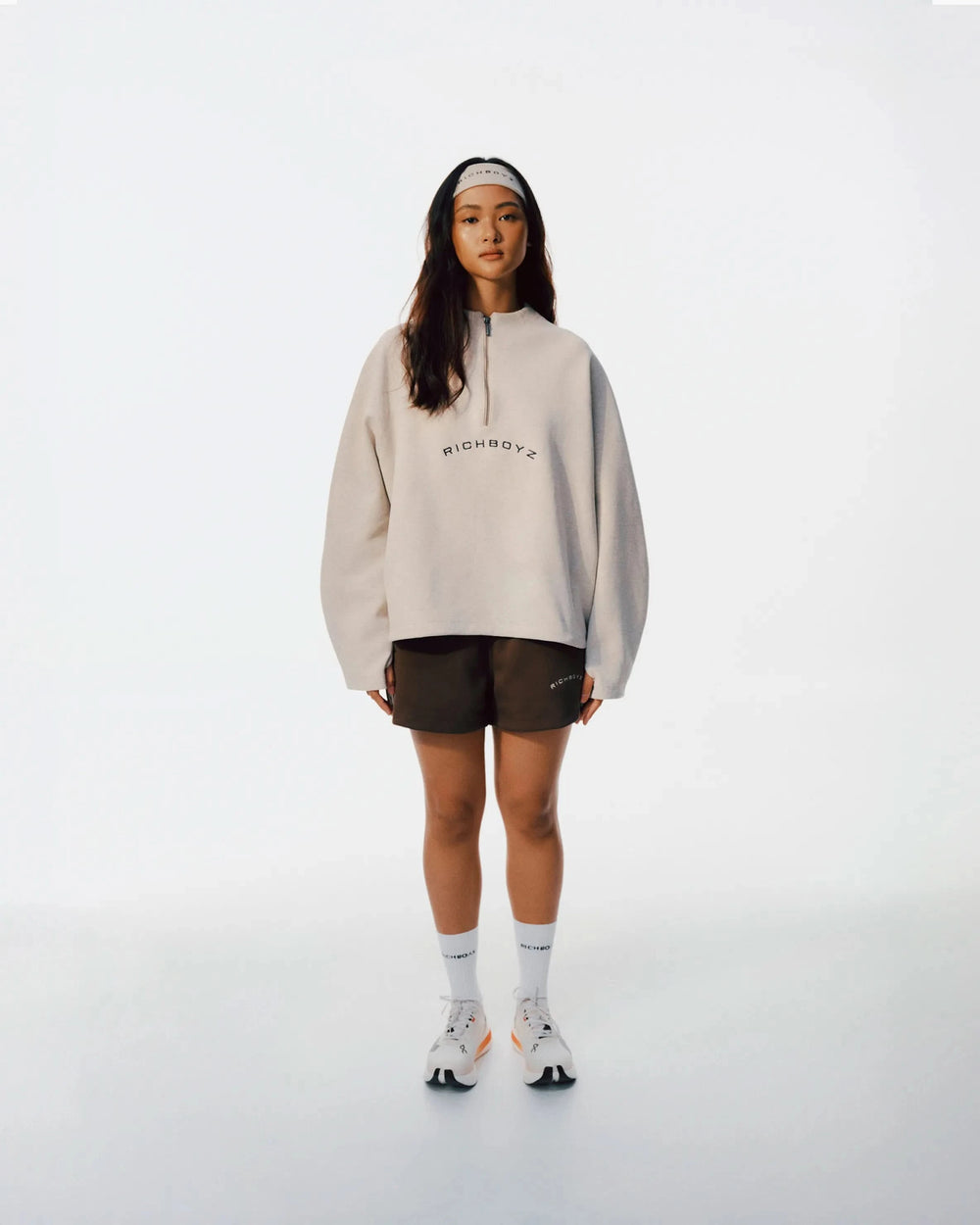 Person wearing a beige hoodie with text, black shorts, and white socks on a white background