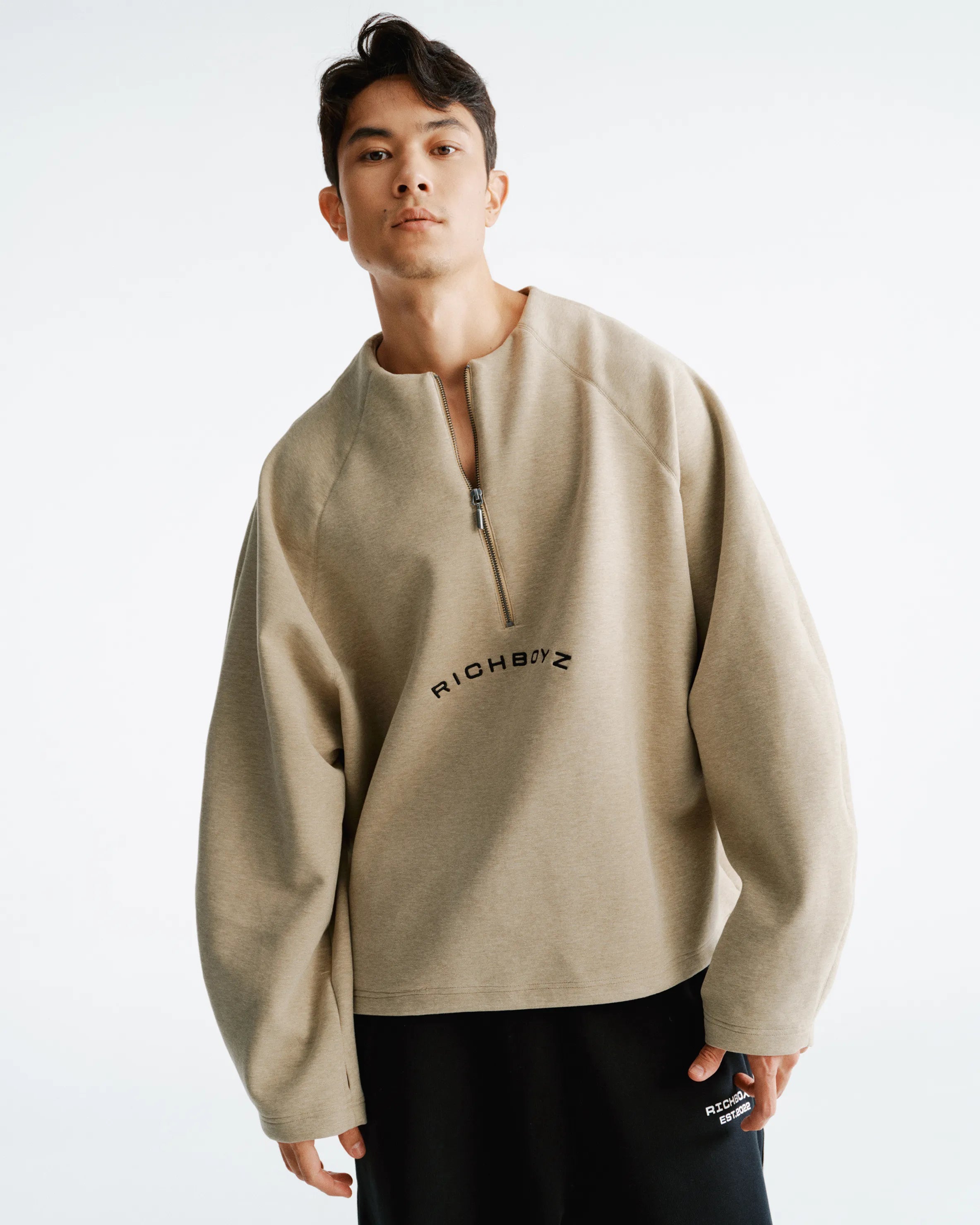 Man wearing a beige sweater with 'RICHBOYZ' branding on a white background