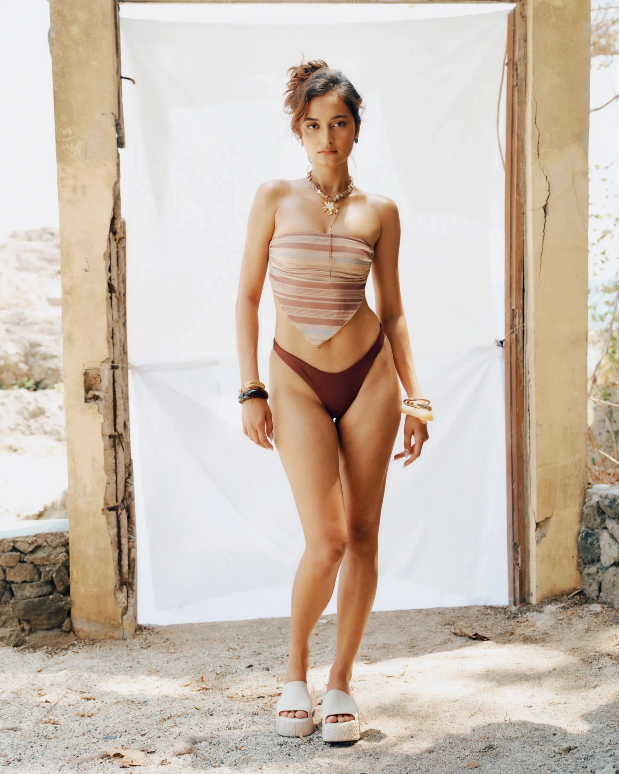 Woman in a strapless bikini standing in front of a white wall with a rustic background.